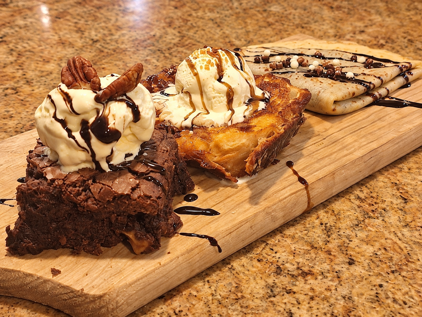 Primer plano de brownie, torrija y crepe con helado sobre una tabla de madera