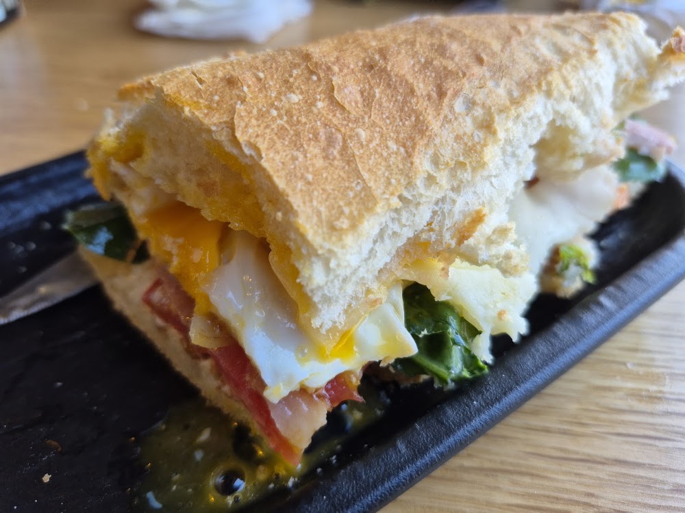 Sándwich tostado con huevo, tomate y hojas verdes